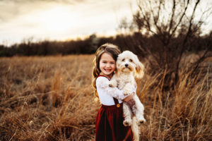 family photographer, little girl holds her little white dog outdoors in a grassy field