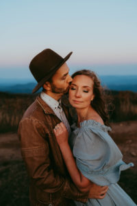 family photographer, man in jacket and hat kisses woman in blue dress
