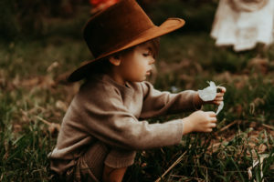 family photography, toddler with cowboy hat examines flower in the grass