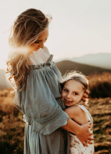family photographer, young smily daughter hugs mother outdoors in a field