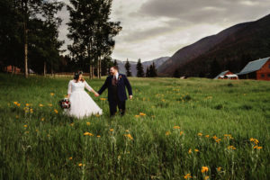 Family Photography, newly wed couple walk through flowery meadow, barn in the distance